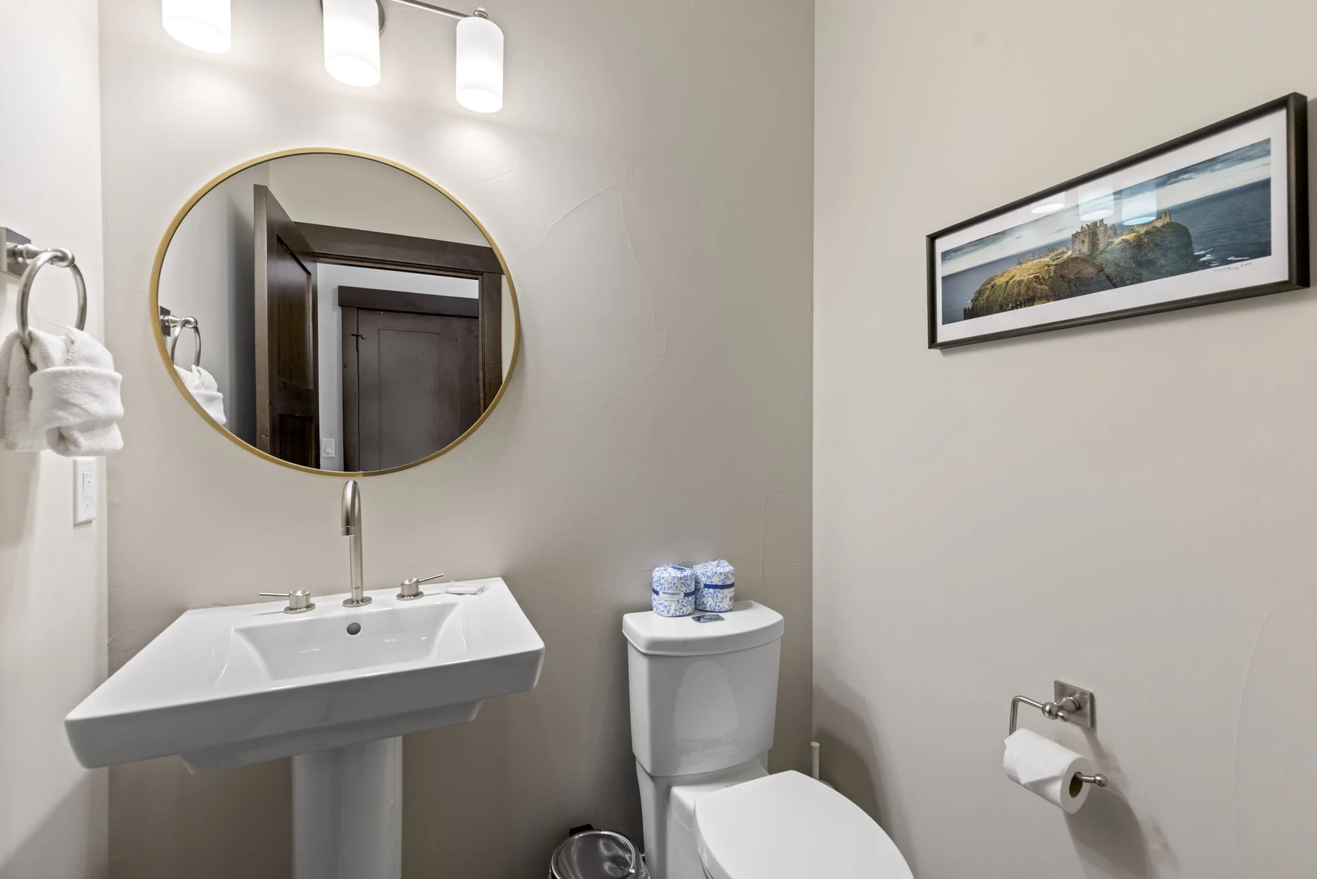 Vendette Peak, bathroom: Compact powder room with a white sink, round mirror, toilet, and framed landscape print, luxury vacation rental in Silverthorne, Colorado