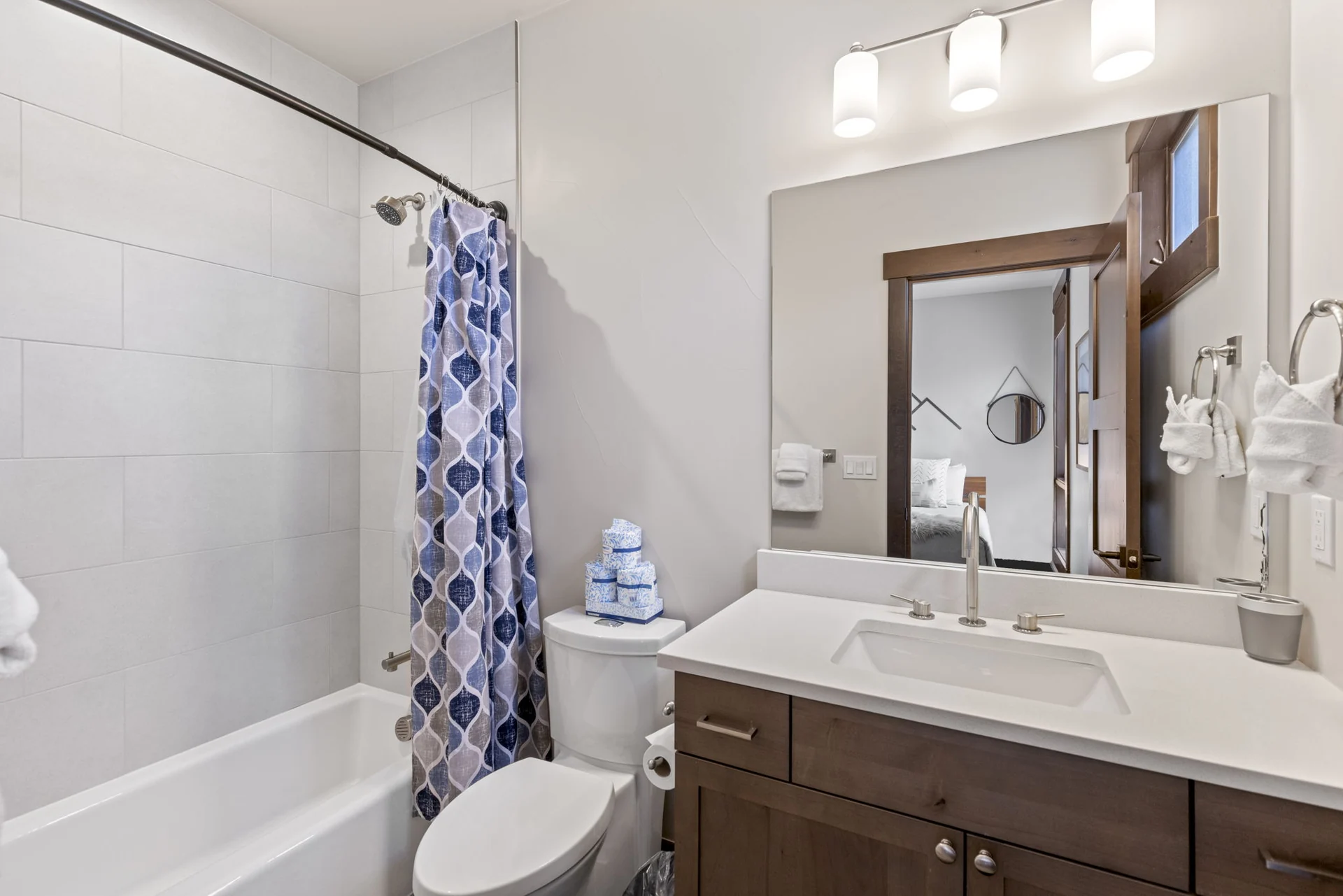 Vendette Peak, bathroom: Bathroom with a tub and patterned shower curtain, toilet, dark wood vanity, and large mirror, luxury vacation rental in Silverthorne, Colorado