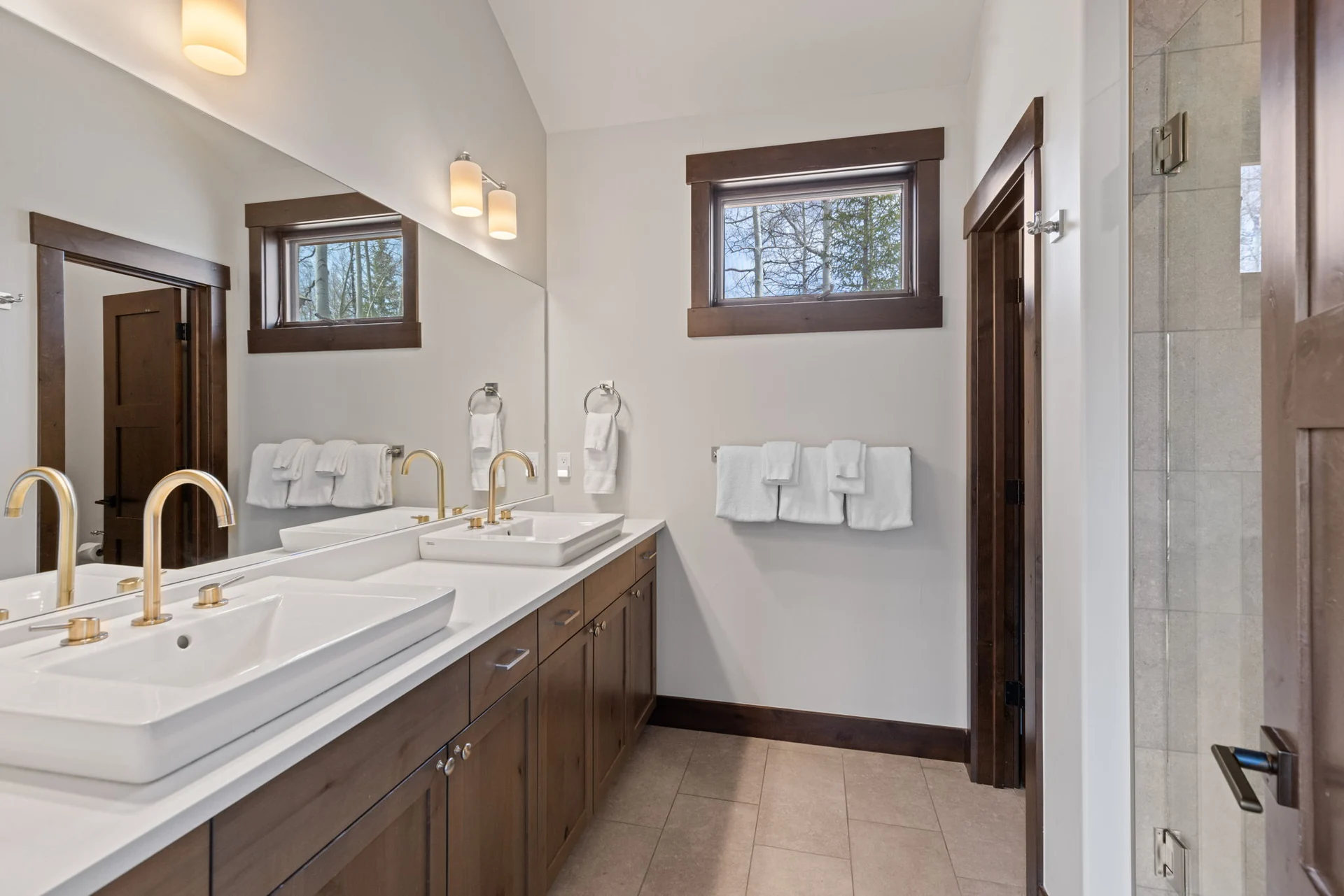 Vendette Peak, bathroom: Long double-sink vanity with gold-toned faucets, dark wood cabinetry, two windows, and a shower edge, luxury vacation rental in Silverthorne, Colorado