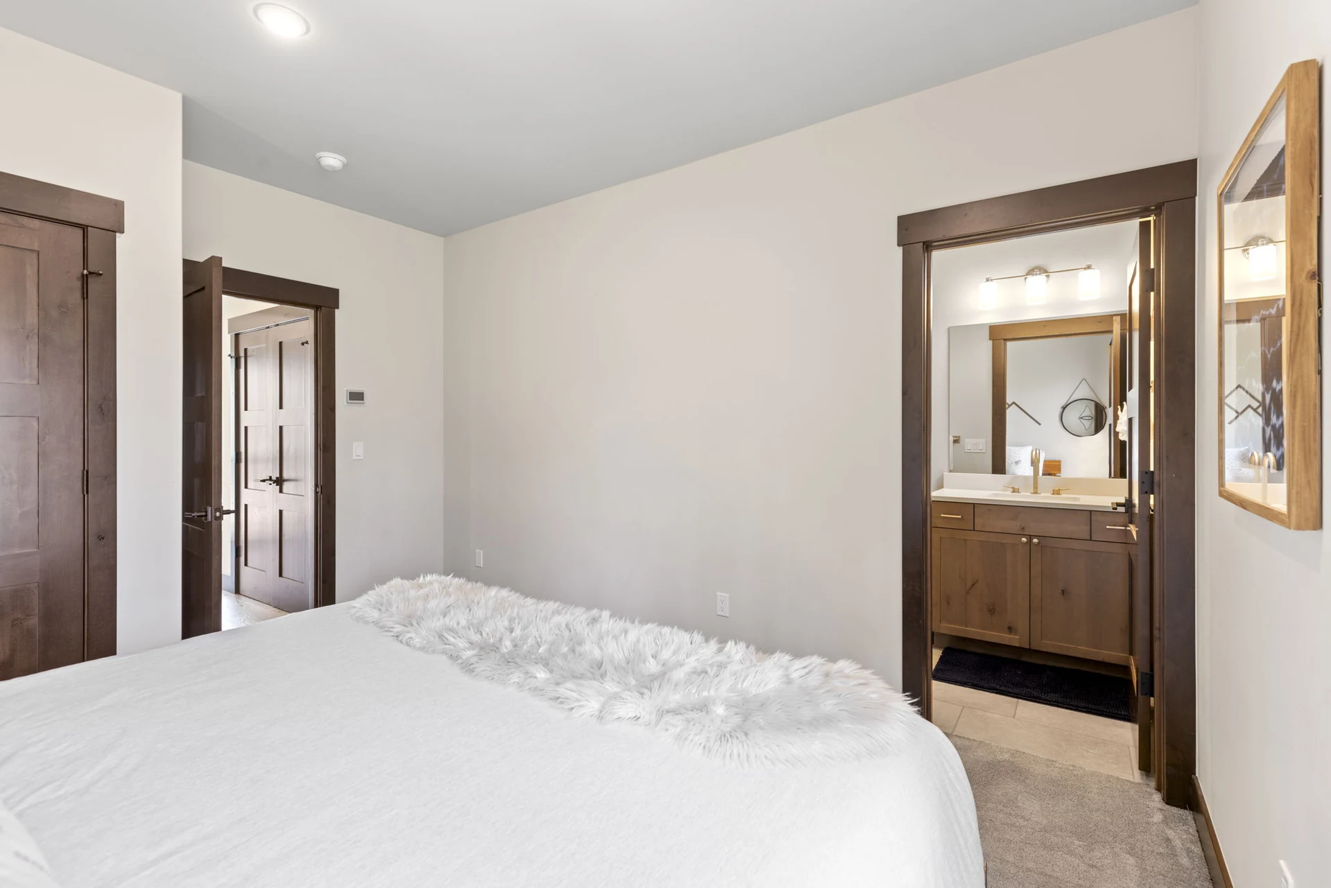 Vendette Peak, bedroom: Reverse view of the white-bedded room, showing dark wood doors and a vanity through an open doorway, luxury vacation rental in Silverthorne, Colorado