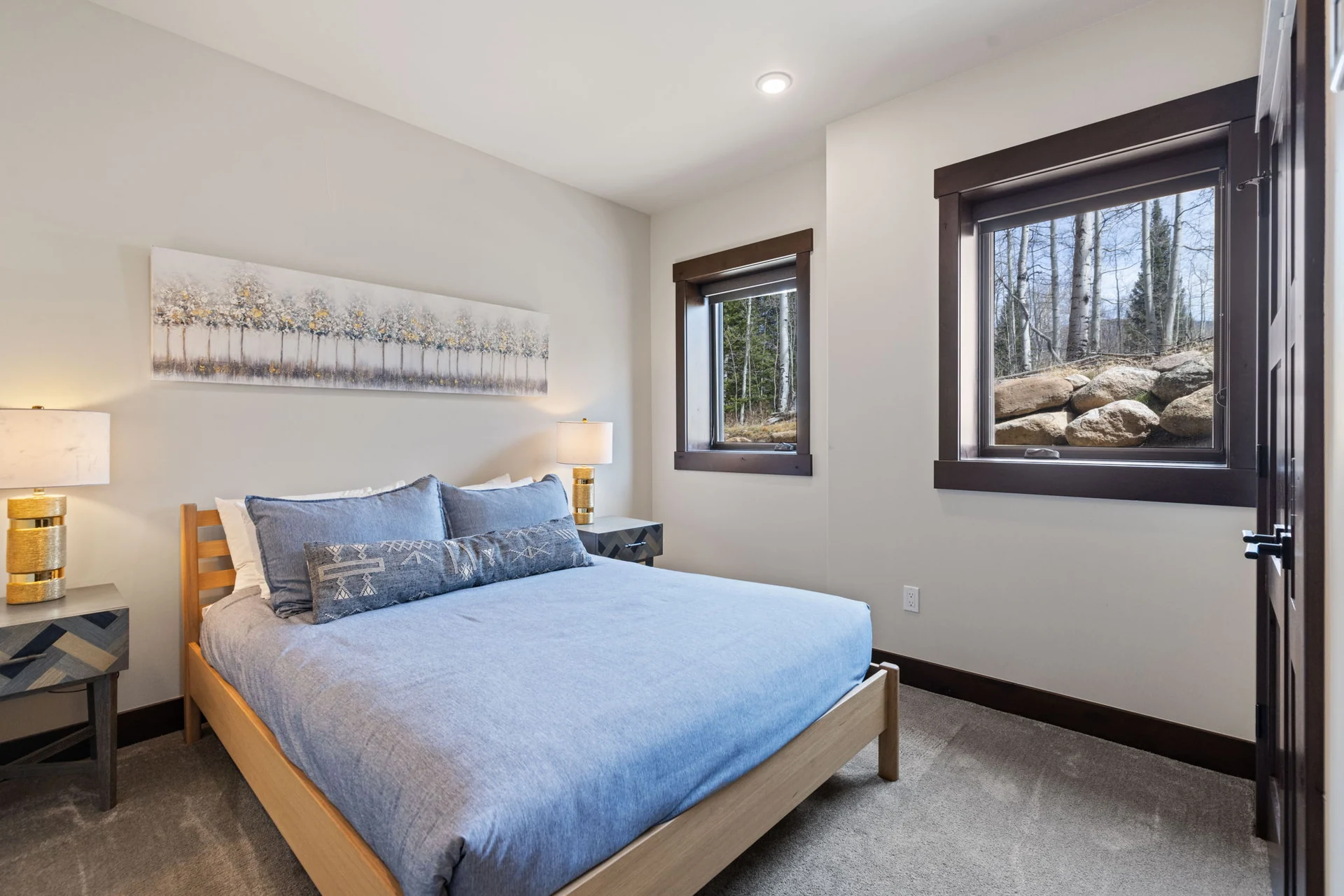 Vendette Peak, bedroom: Bedroom with a blue coverlet, bedside lamps, two windows, and a long tree-print artwork above the bed, luxury vacation rental in Silverthorne, Colorado