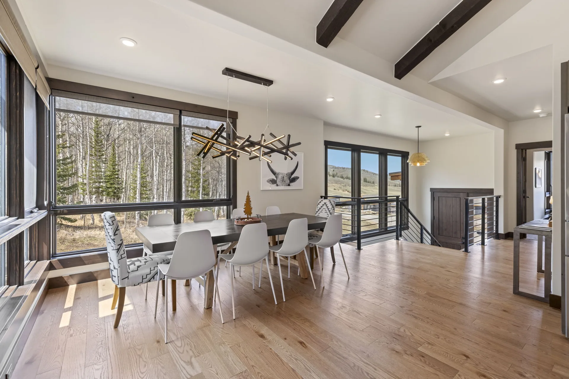 Vendette Peak, dining room: Window-side view of the dining table, patterned end chairs, dark ceiling beams, and forest outside, luxury vacation rental in Silverthorne, Colorado