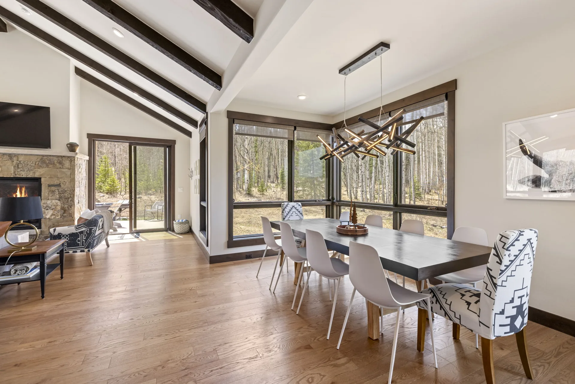 Vendette Peak, dining room: Dining table and white chairs beneath a branching pendant, with large windows and the stone fireplace nearby, luxury vacation rental in Silverthorne, Colorado