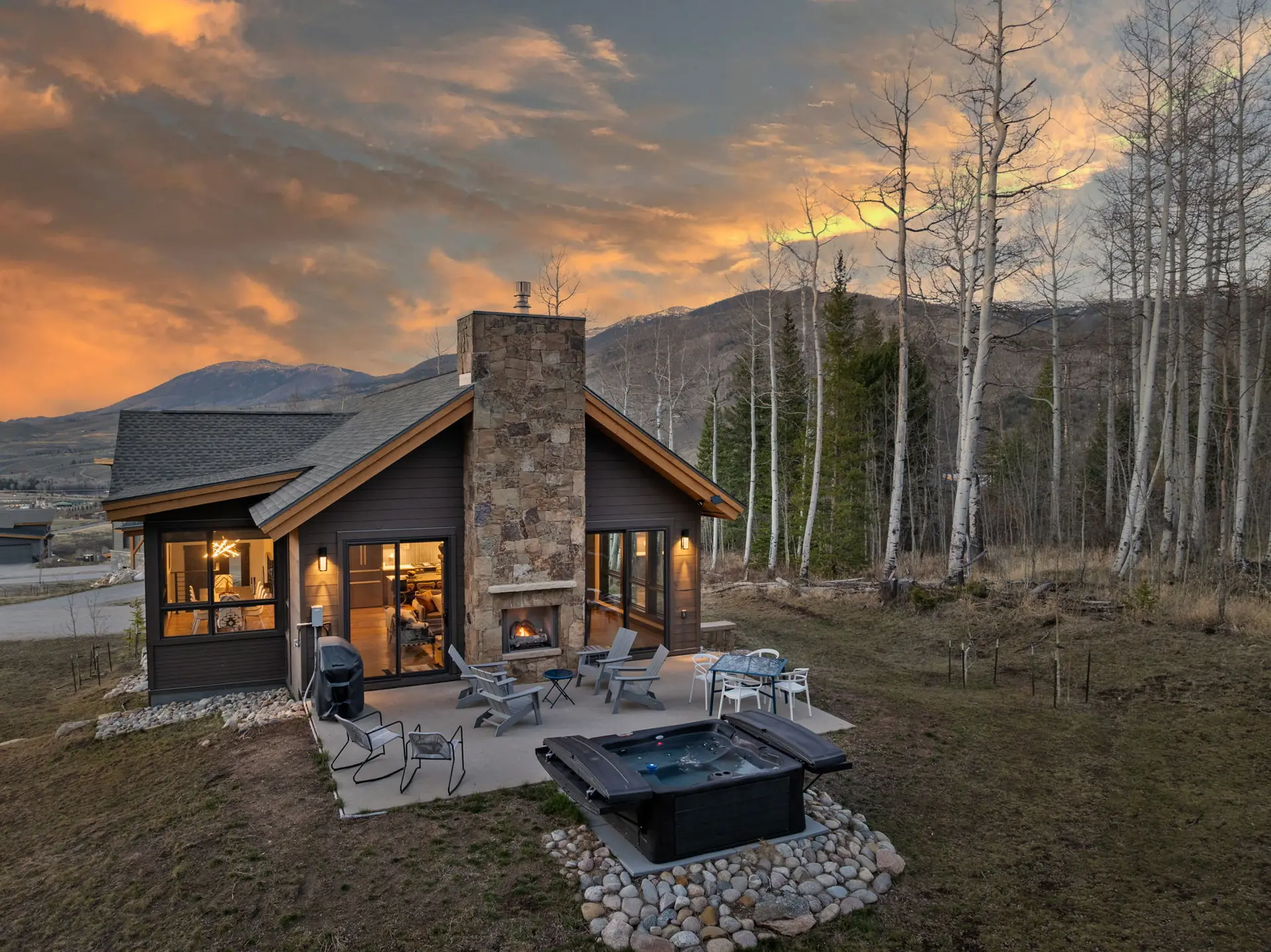 Vendette Peak, exterior: Angled sunset view of the home, its stone chimney, patio furniture, hot tub, and surrounding aspens, luxury vacation rental in Silverthorne, Colorado