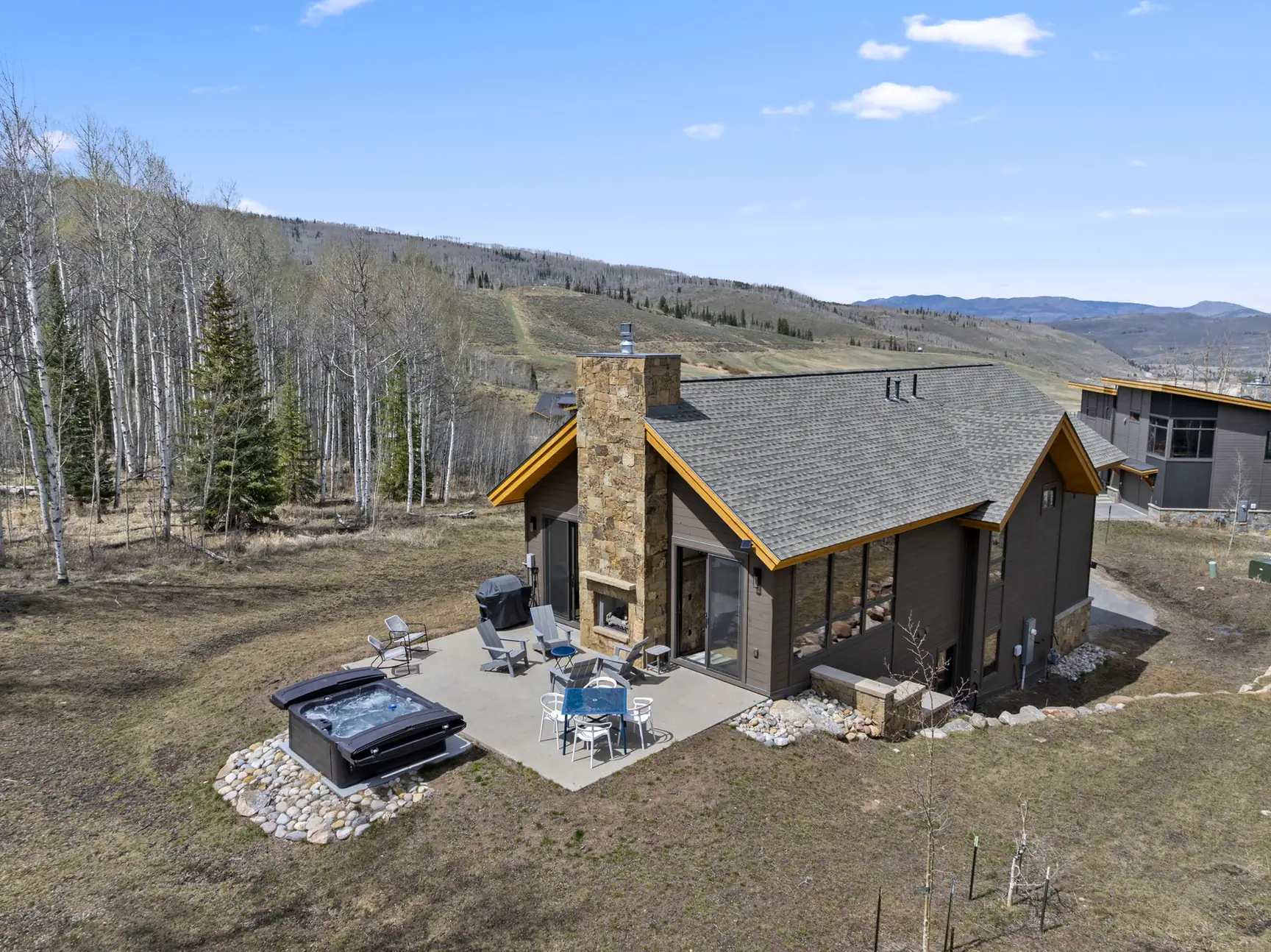 Vendette Peak, exterior: Elevated view of the roof, stone chimney, patio, hot tub, and nearby hillside in daylight, luxury vacation rental in Silverthorne, Colorado