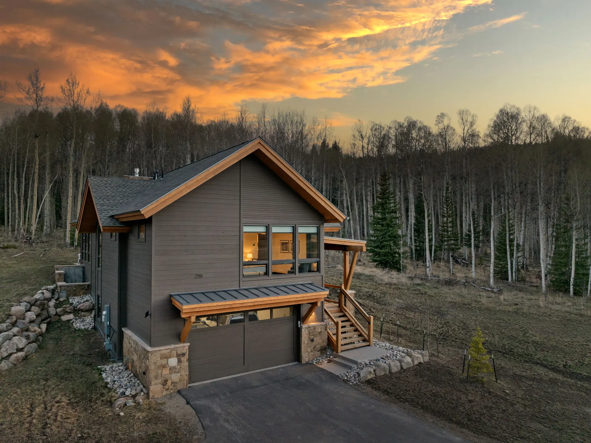 Vendette Peak, exterior: Closer drive-side view of the garage, wood-railed entry steps, and warmly lit windows, luxury vacation rental in Silverthorne, Colorado