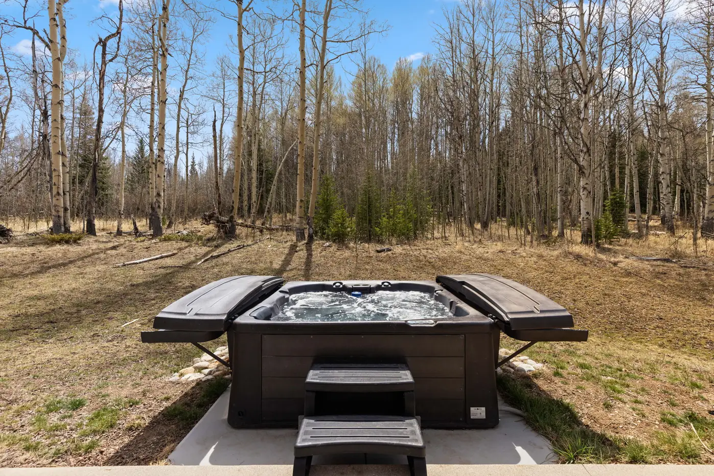 Vendette Peak, hot tub: Front view of the square hot tub and entry step, with leafless aspens beyond the patio, luxury vacation rental in Silverthorne, Colorado