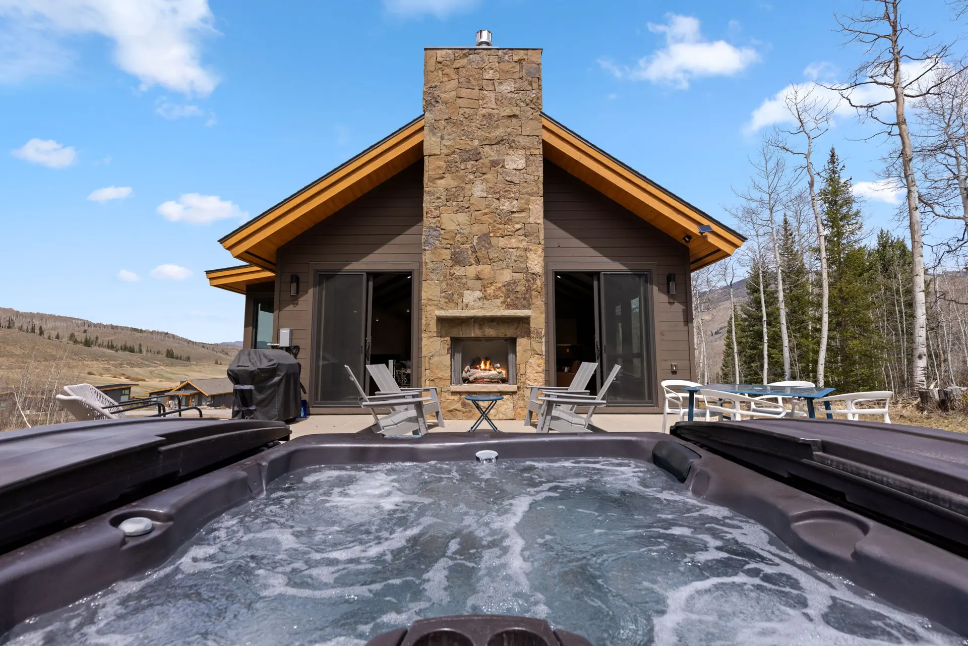 Vendette Peak, hot tub: Bubbling hot tub facing the home, its stone chimney, glass doors, and outdoor seating, luxury vacation rental in Silverthorne, Colorado