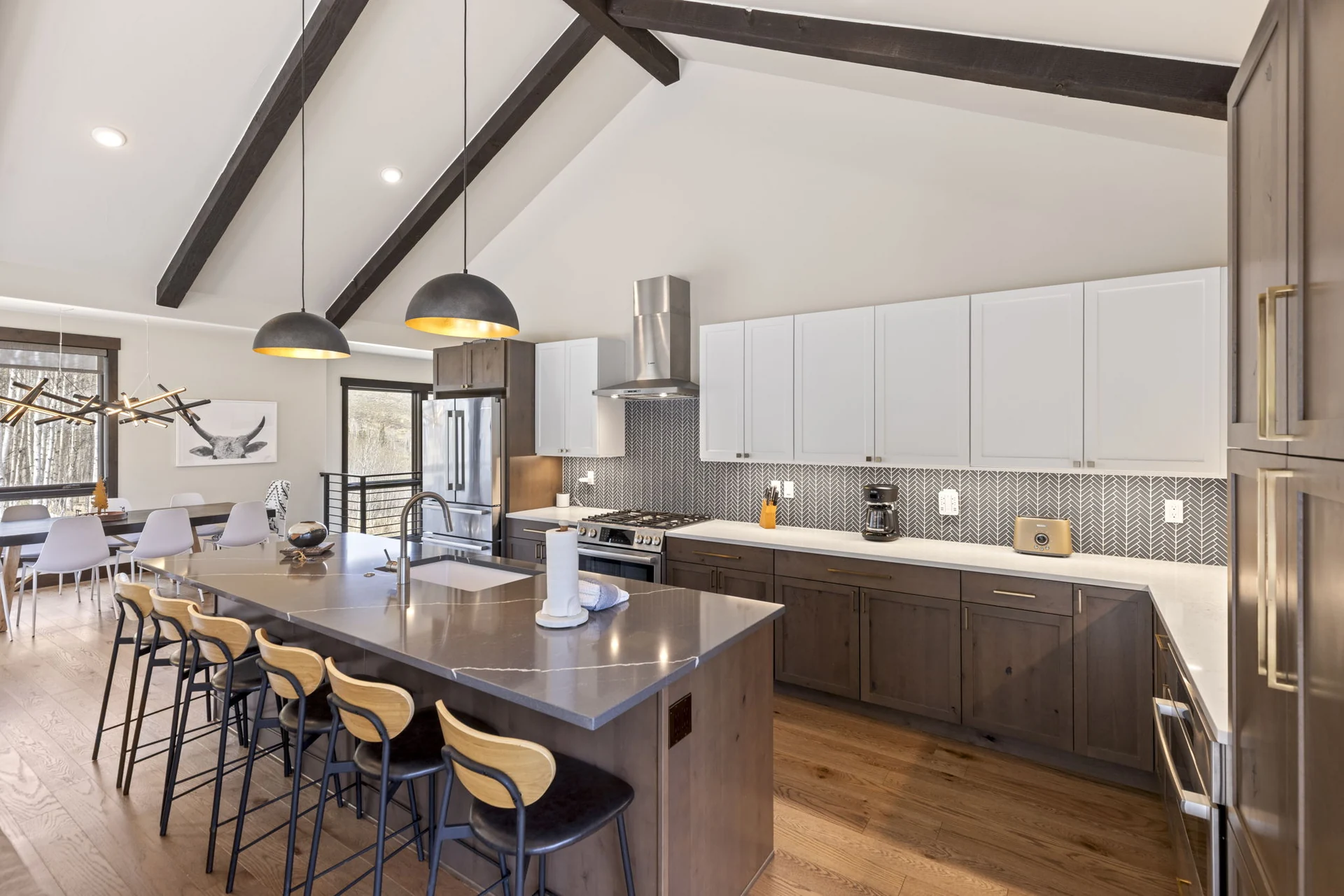 Vendette Peak, kitchen: Kitchen work wall with white upper cabinets, dark lower cabinets, a range hood, and an island lined with stools, luxury vacation rental in Silverthorne, Colorado