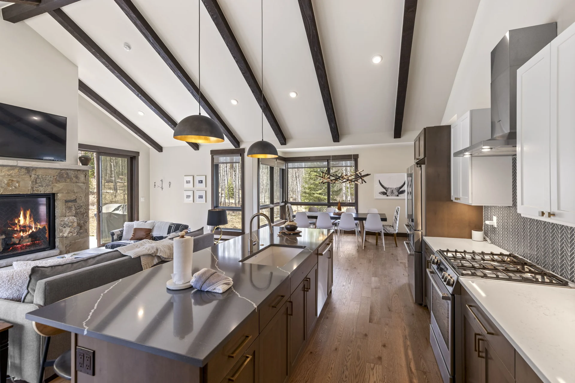 Vendette Peak, kitchen: View past the island sink toward the cooktop, fireplace, sofas, and forest-facing windows, luxury vacation rental in Silverthorne, Colorado