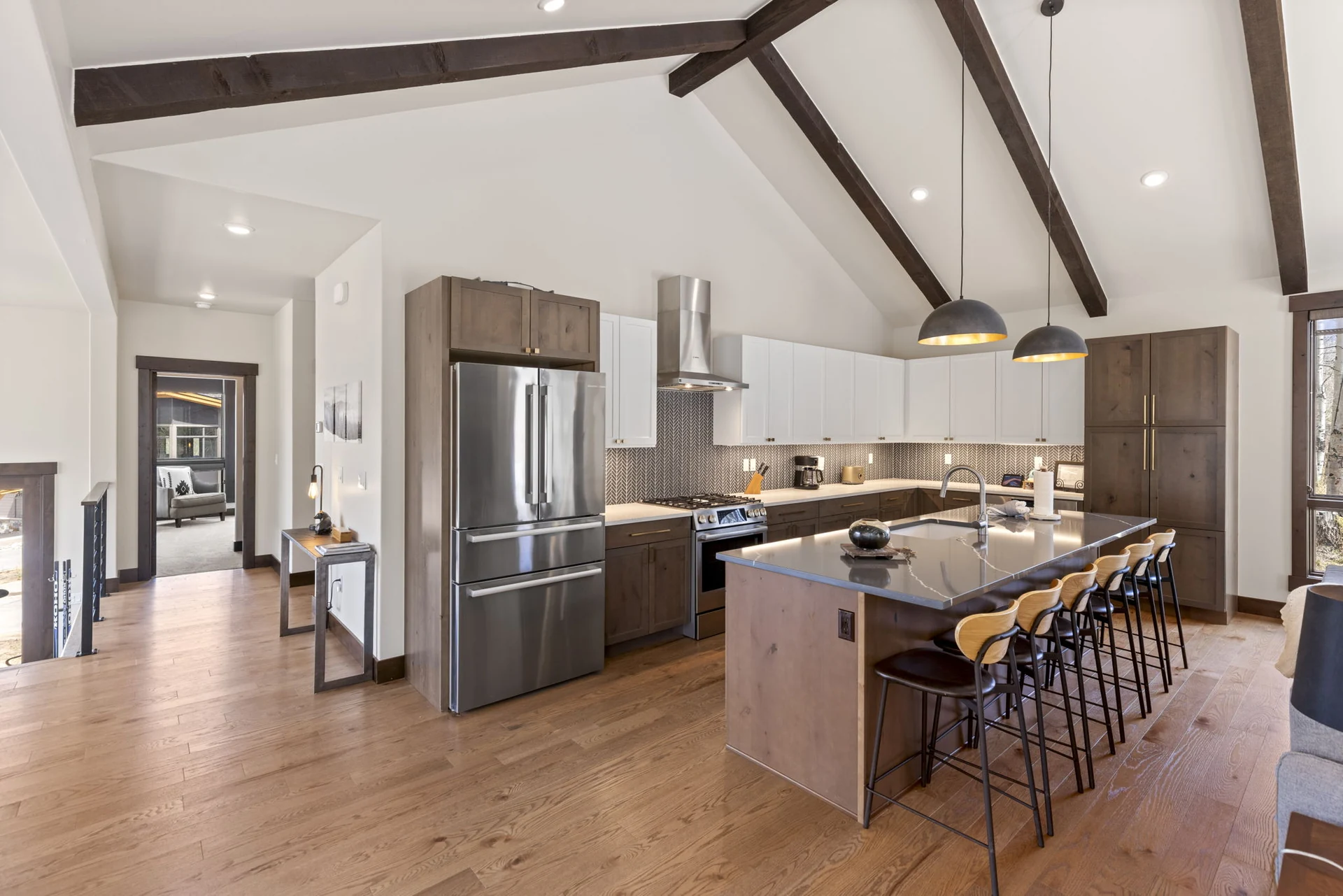 Vendette Peak, kitchen: Wide kitchen view with the refrigerator, island seating, white and dark cabinetry, and exposed beams, luxury vacation rental in Silverthorne, Colorado