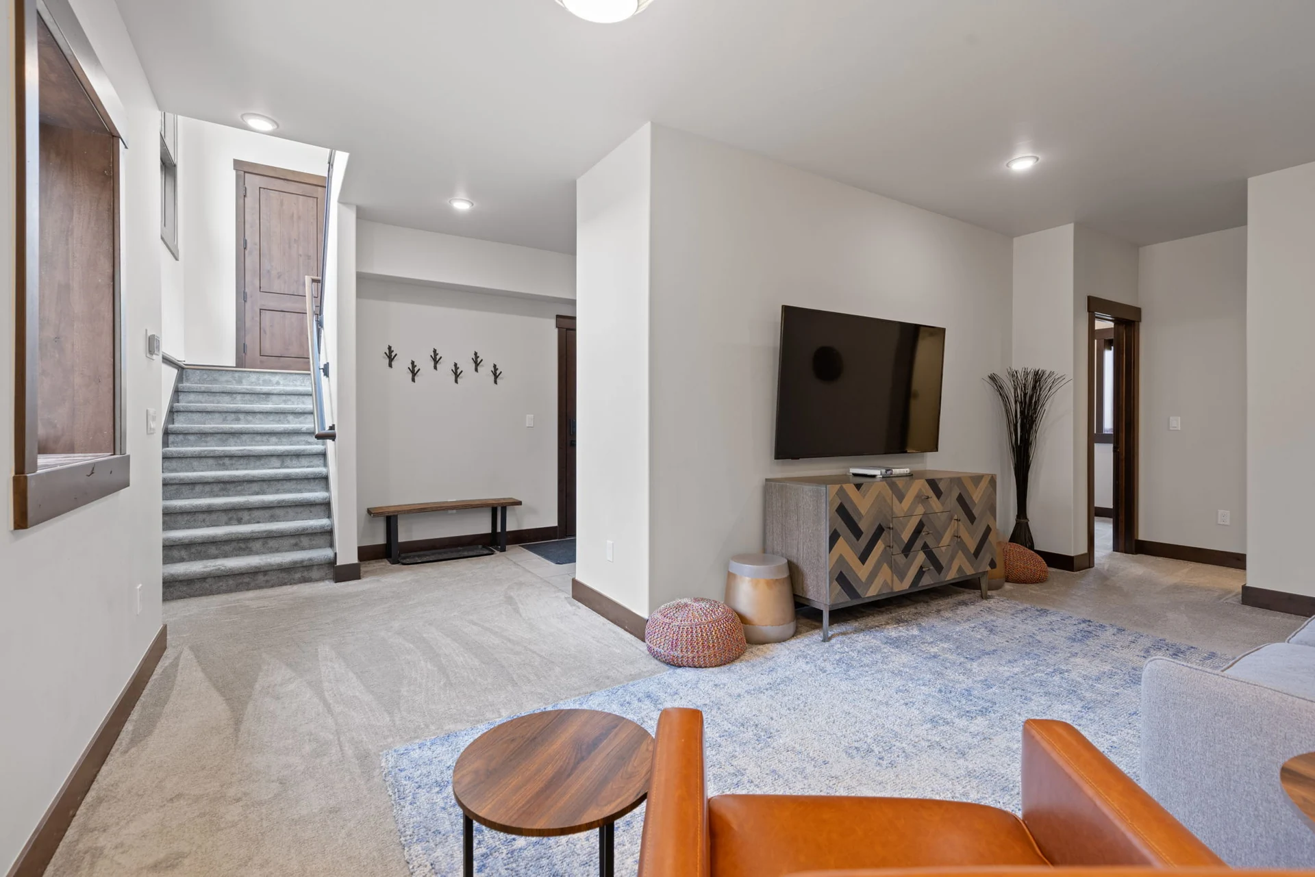 Vendette Peak, living room: Separate sitting room with an orange armchair, large rug, TV, and stairway by the entry, luxury vacation rental in Silverthorne, Colorado