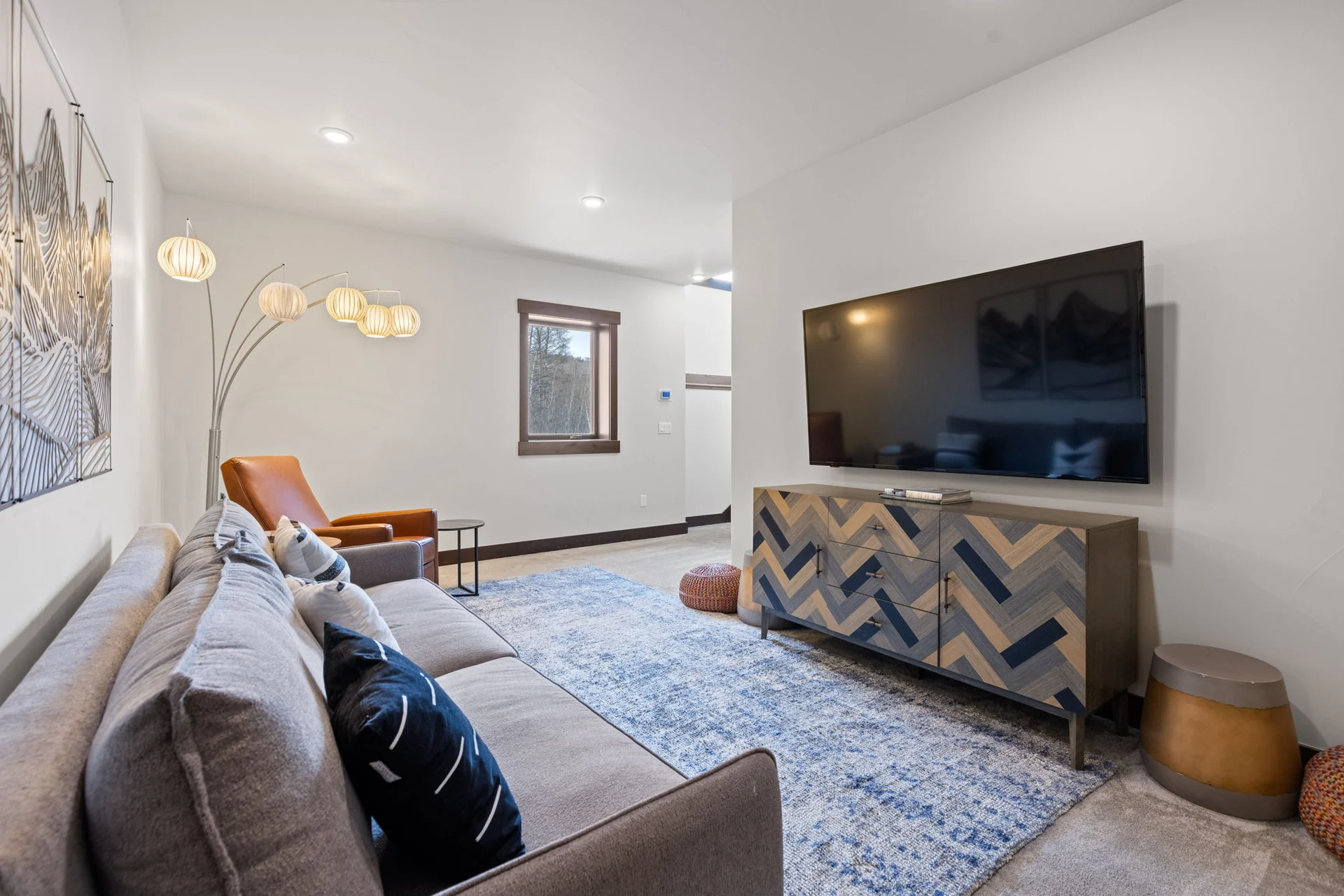 Vendette Peak, living room: Closer view of the sitting room's sofa, orange armchair, multi-globe lamp, TV, and patterned console, luxury vacation rental in Silverthorne, Colorado
