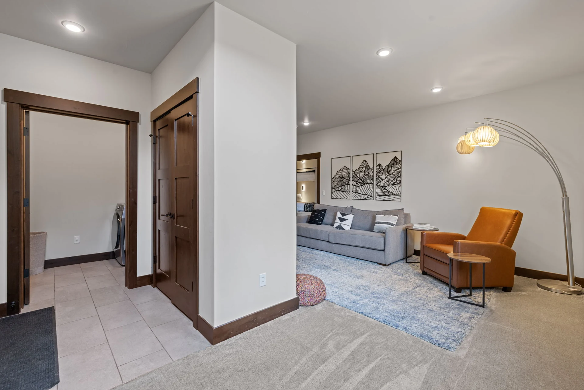 Vendette Peak, living room: View into the sitting area from the tiled hallway, with wood doors, gray sofa, orange chair, and TV, luxury vacation rental in Silverthorne, Colorado