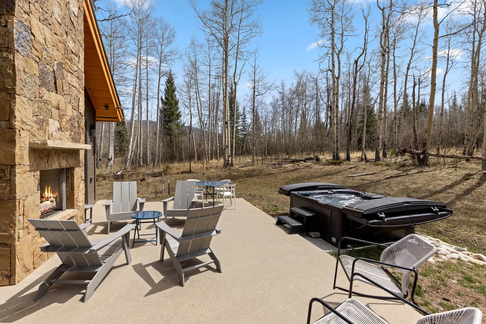 Vendette Peak, patio: Stone-lined patio with lounge chairs, a small table, hot tub, and open view toward the trees, luxury vacation rental in Silverthorne, Colorado