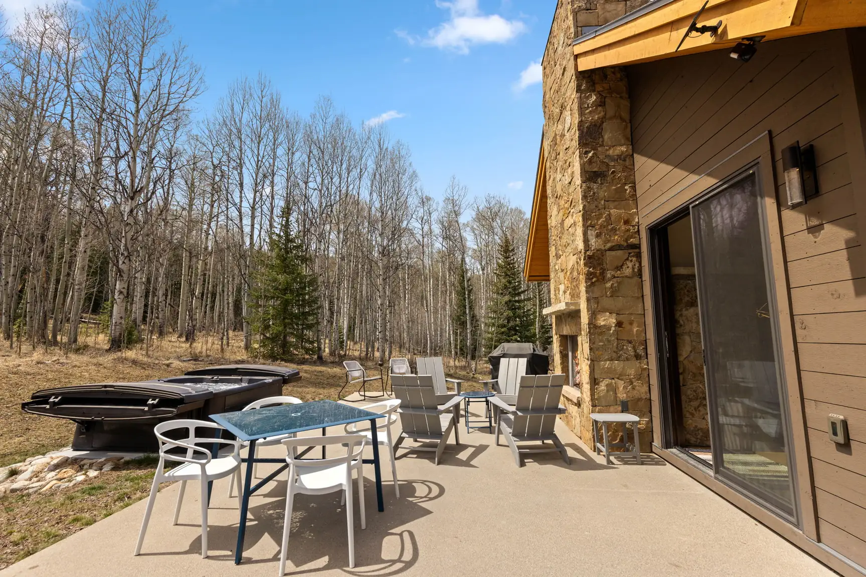 Vendette Peak, patio: Outdoor dining table and white chairs beside the sliding door, with lounge seating and the hot tub nearby, luxury vacation rental in Silverthorne, Colorado